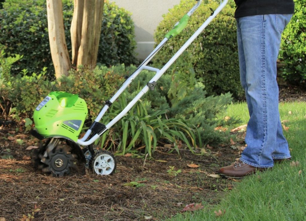 An electric cultivator in a garden bed, with a person who is preparing to use it.